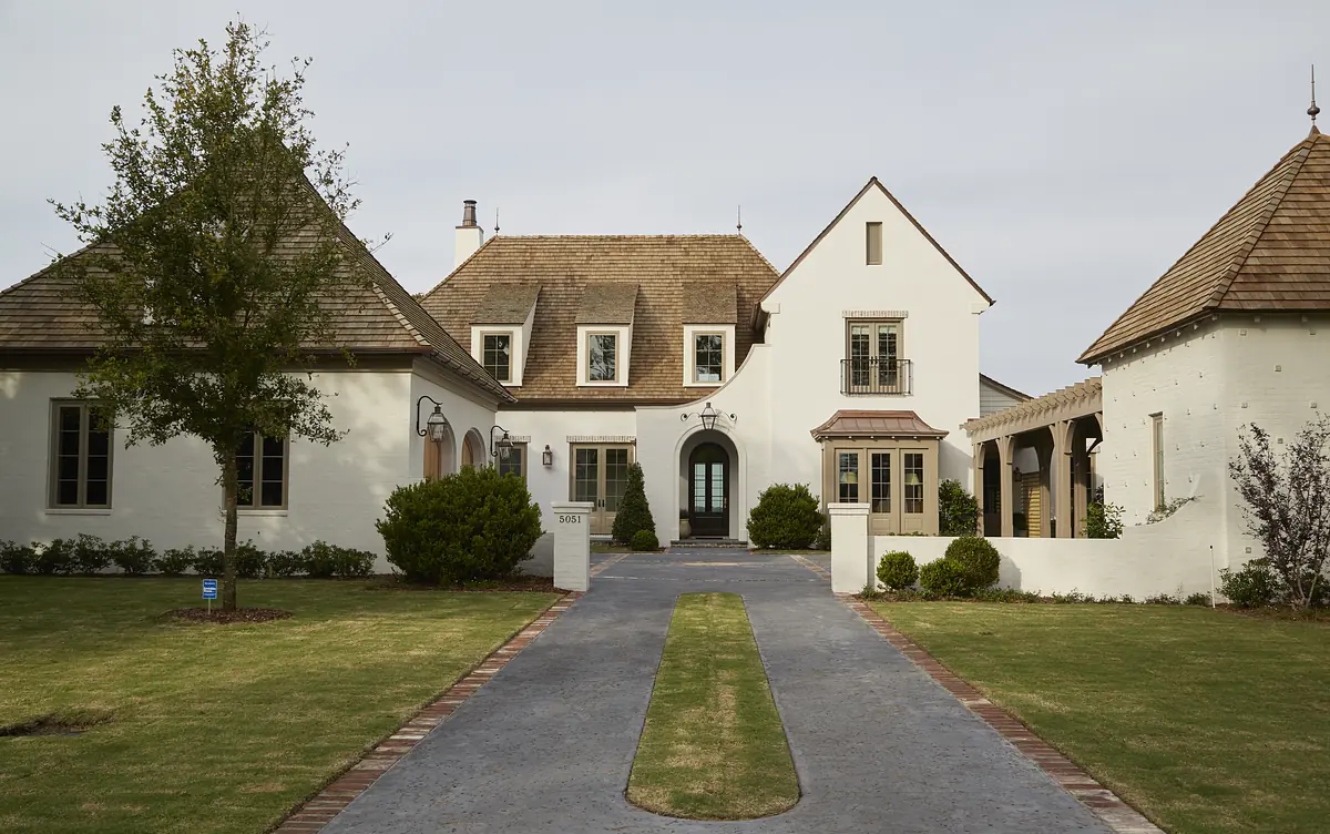 Front exterior of a house with stone pathway, manicured grass, multiple gabled roofs, and white stucco walls.
