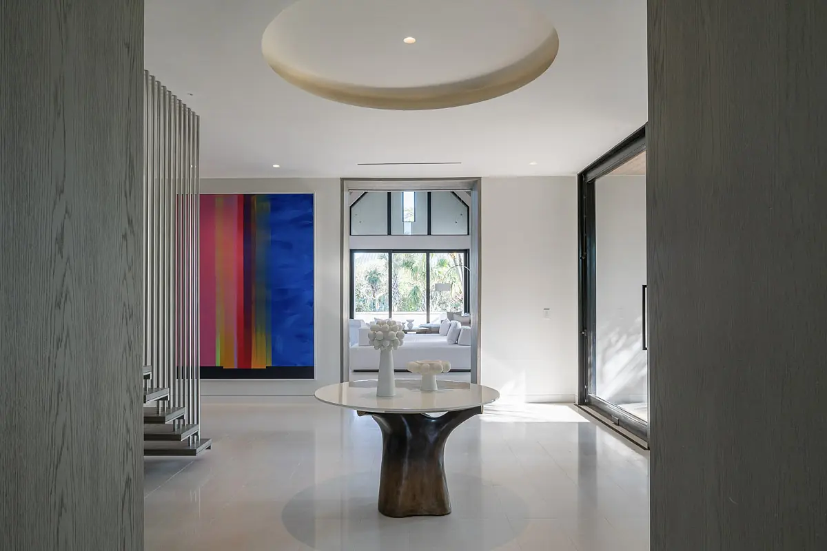 Foyer with round table, large colorful artwork, staircase with metal railings, and large windows for natural light