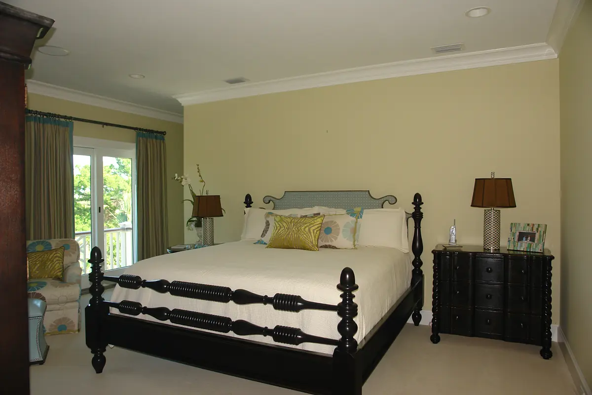 Bedroom with four-poster bed, nightstands, lamps, chair, and large windows.