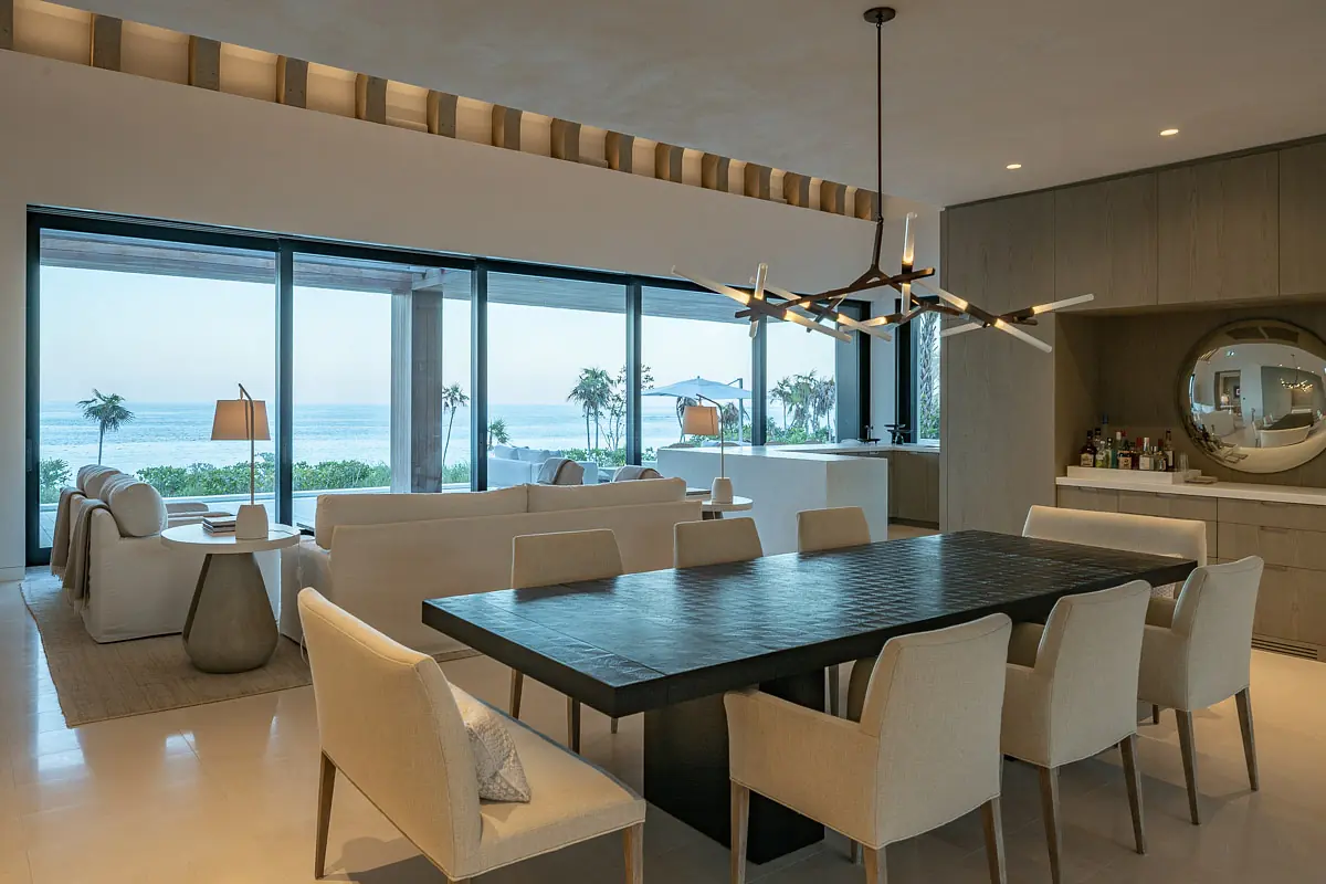Dining room with black table, white chairs, circular mirror, built-in bar, and ocean view windows