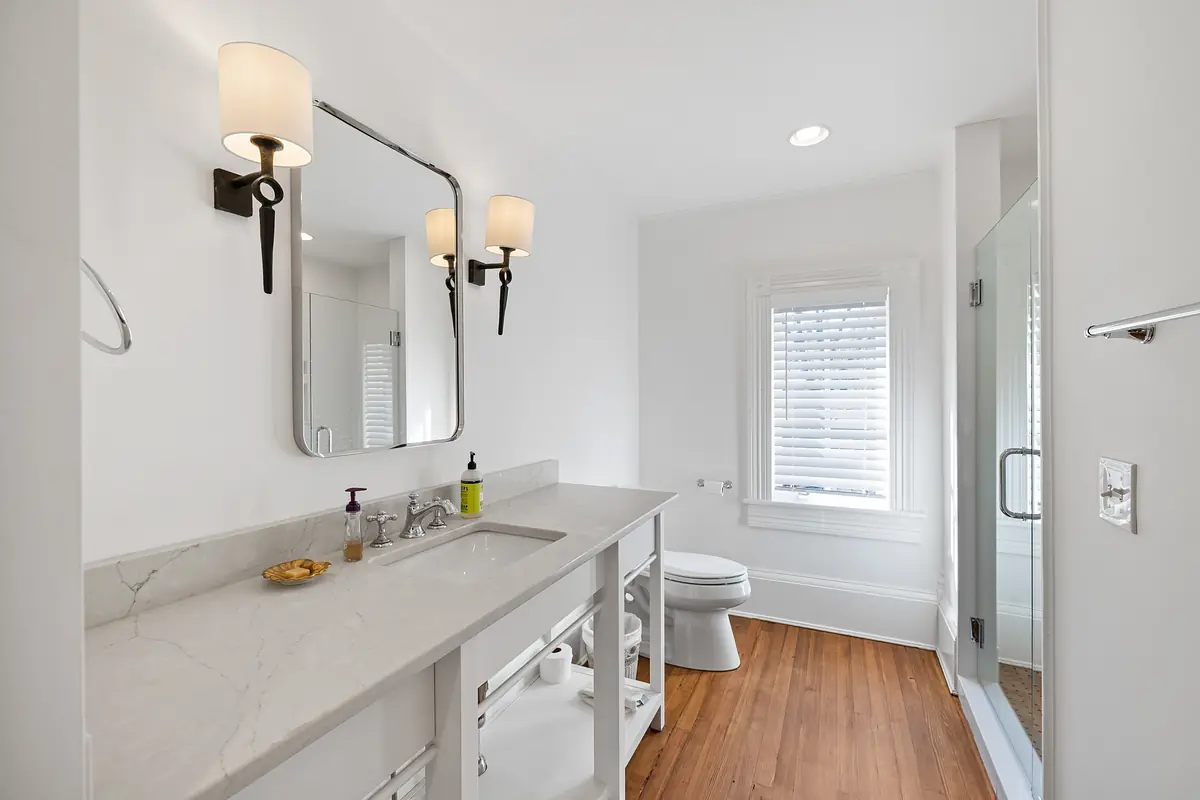 Bathroom with marble vanity, dual sinks, large mirror, toilet, and glass shower.