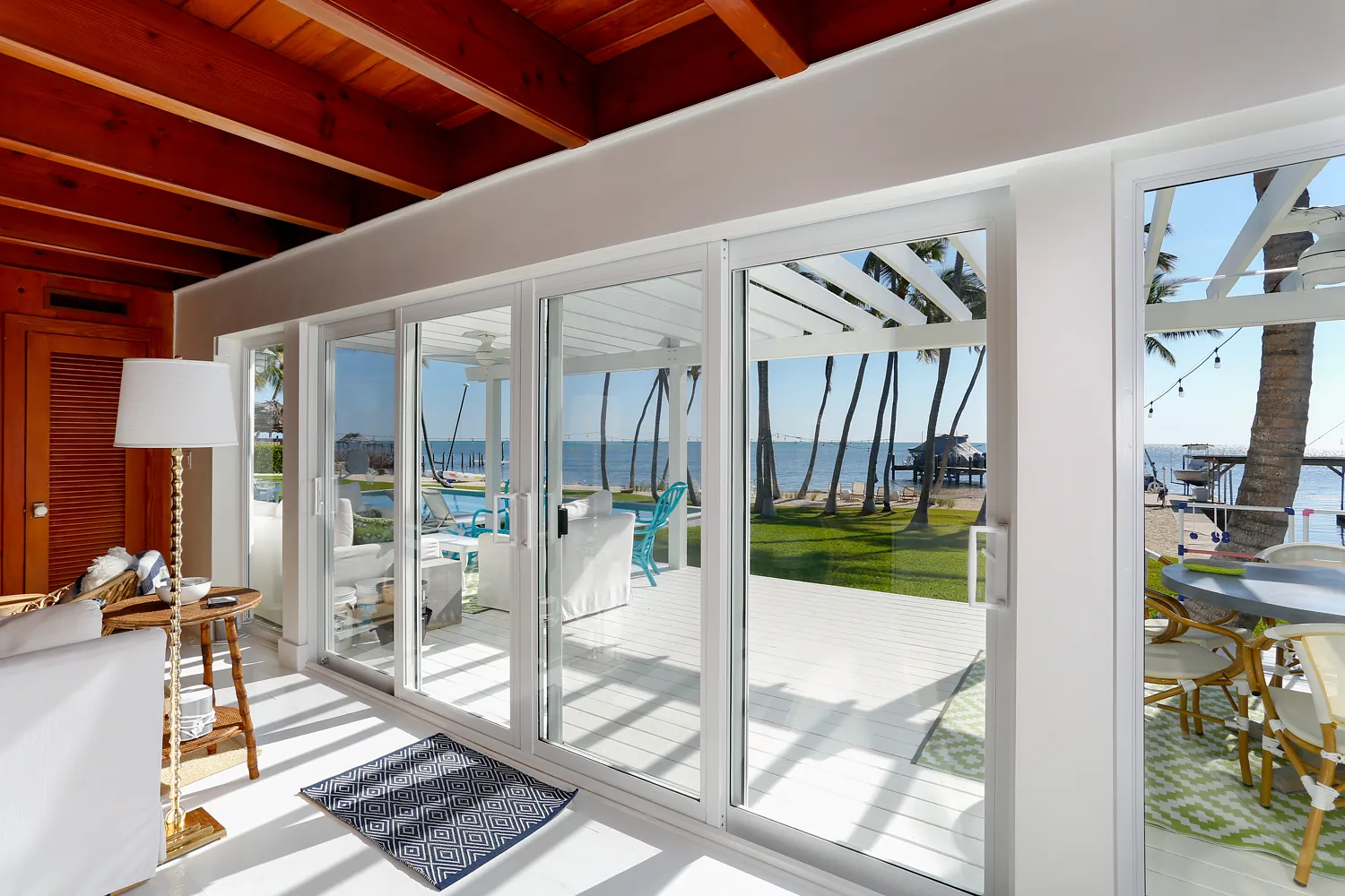 Living room with sliding glass doors, white sofas, coffee table, and blue accent chairs with beach view.