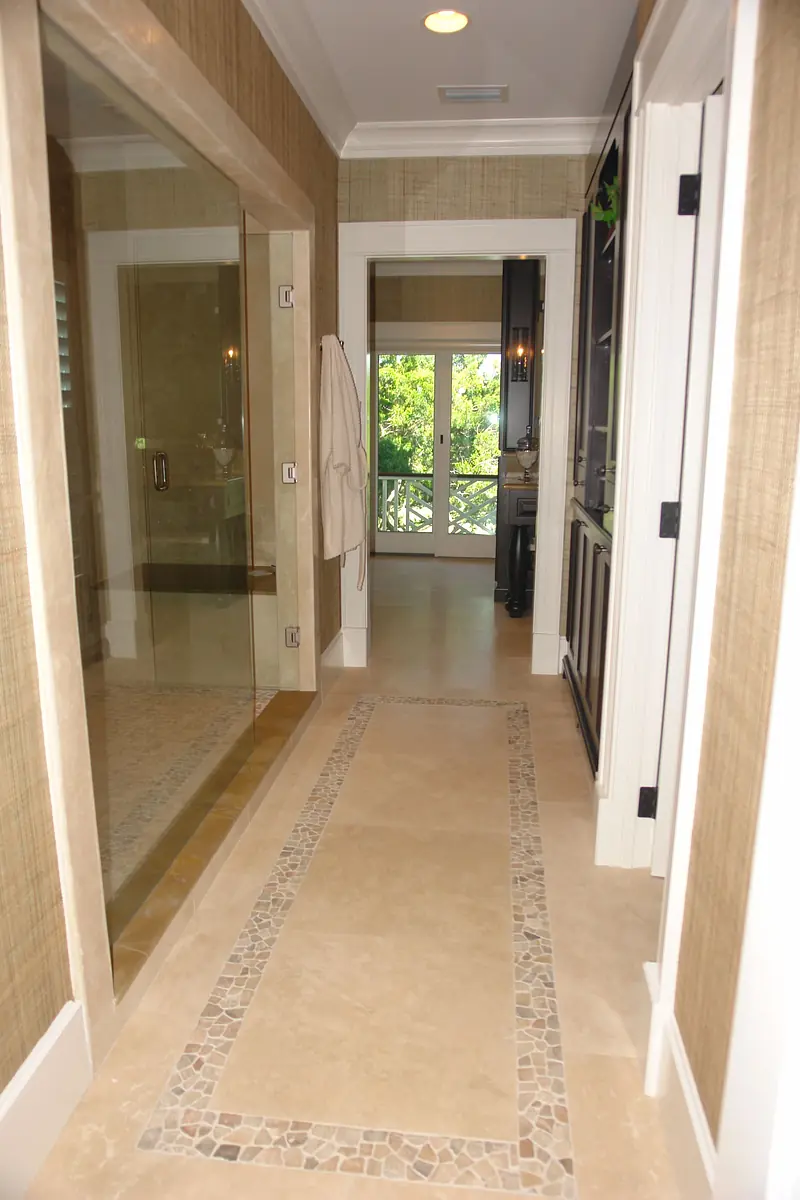 Bathroom hallway with glass shower, stone flooring, and doors to shower area and exterior balcony.