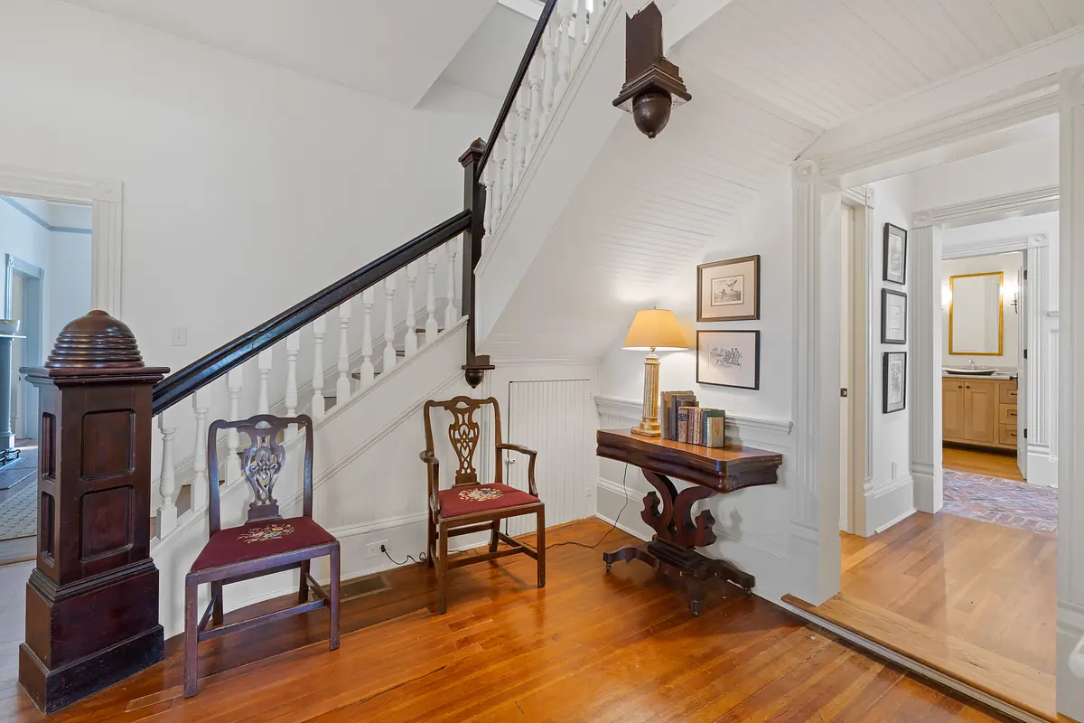 Foyer with staircase, wooden chairs, side table, hardwood floor, and wall art.