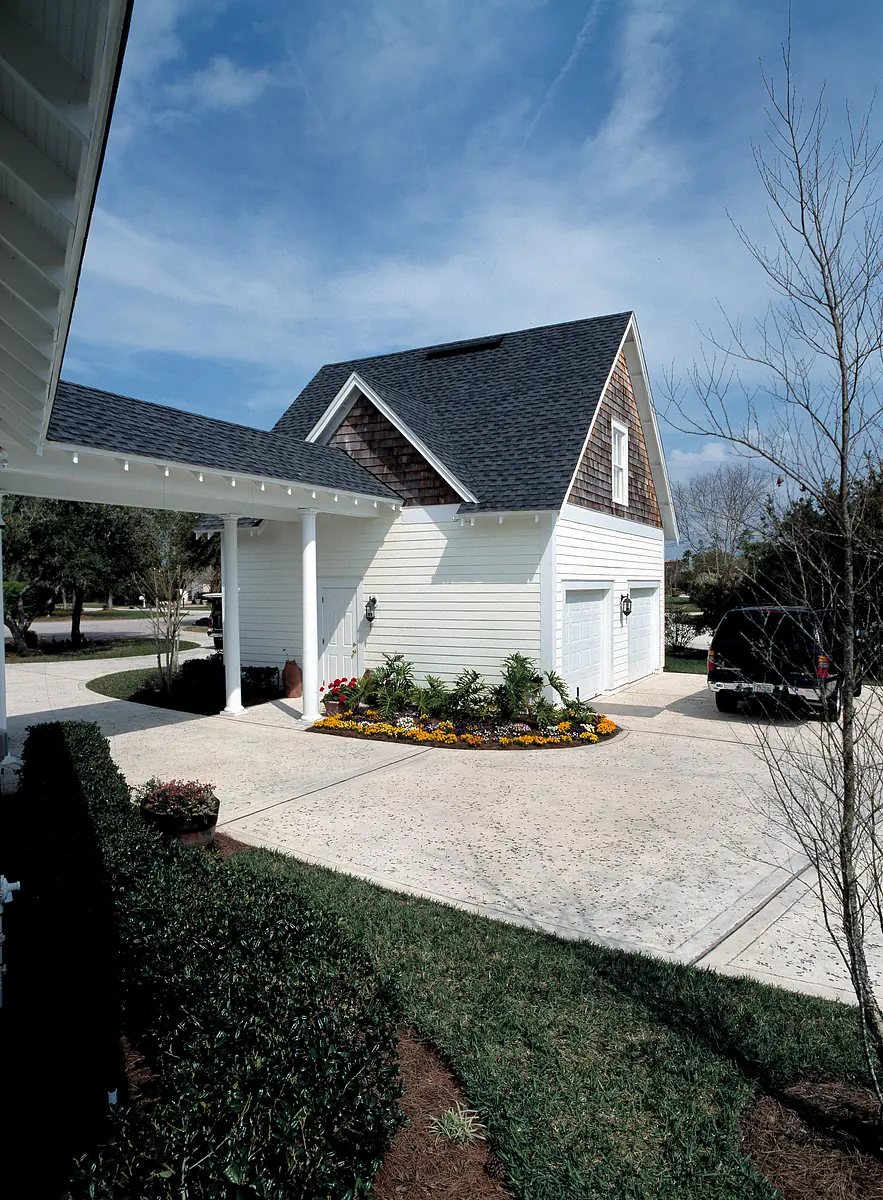 Exterior front view of a white house with gray roof, garage door, driveway, and flower beds.