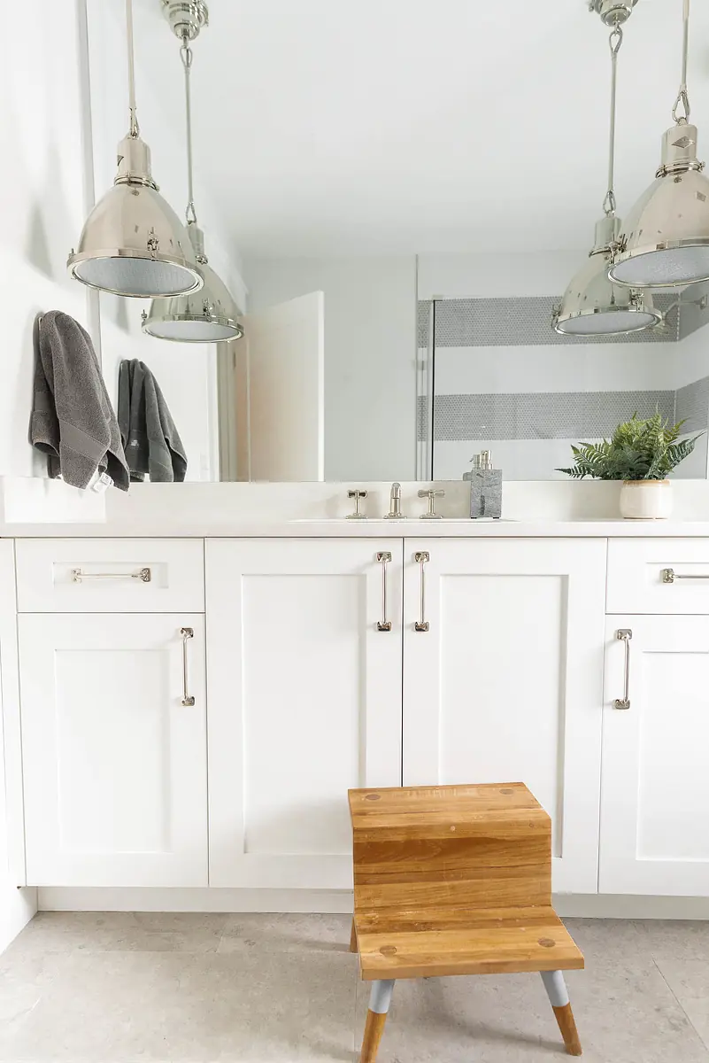 Bathroom with white vanity, wooden step stool, gray striped towels, and glass shower partition