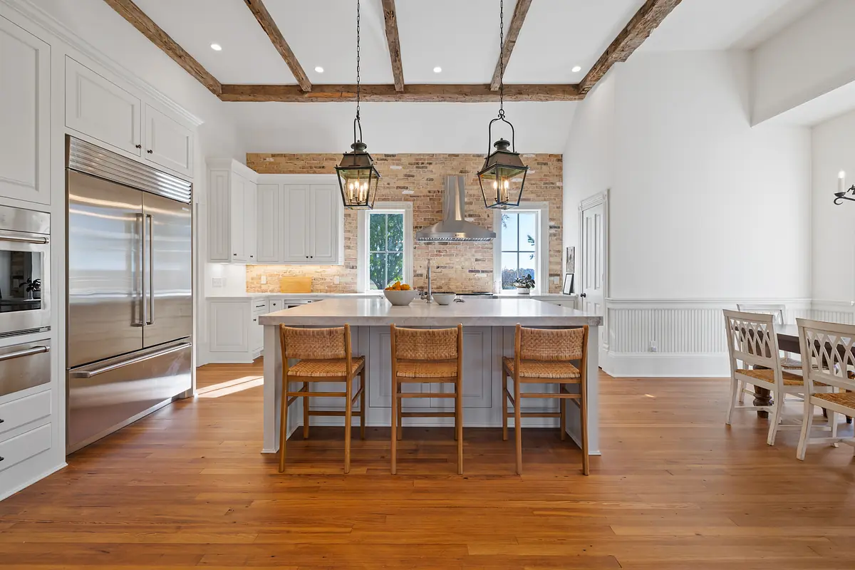 Kitchen with island, barstools, brick wall, white cabinetry, and wooden flooring.