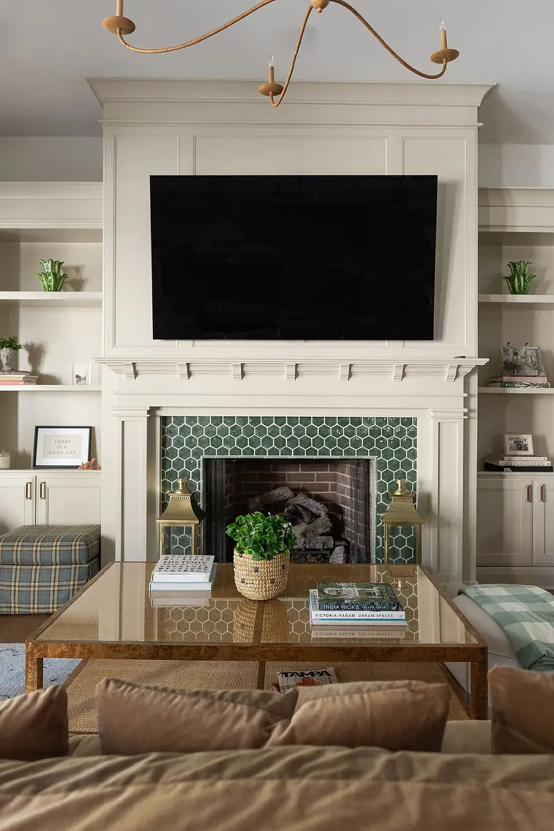 Living room with coffee table, beige sofa, large TV, stone fireplace, and built-in shelving.