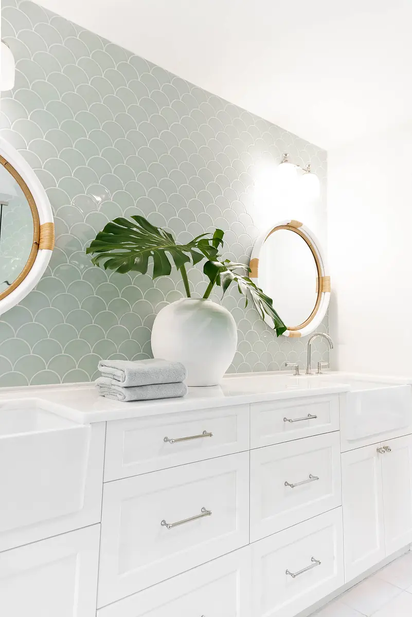Bathroom with double sink vanity, green tile backsplash, circular mirrors, and a potted plant on the countertop.