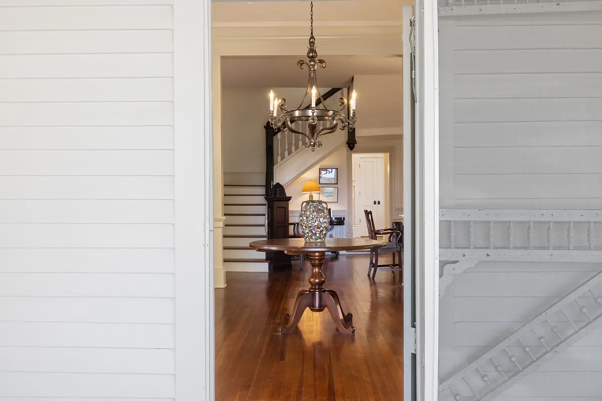 Foyer with round wooden table, vase, chandelier, staircase, and hardwood flooring.