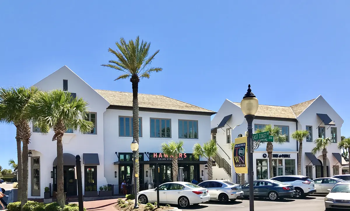 Exterior view of a two-story commercial building with white facade, wood accents, palm trees, and parked cars.