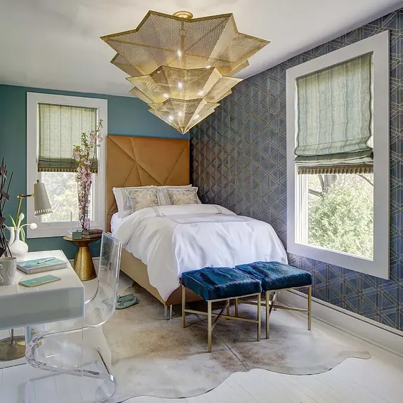 Bedroom with queen bed, acrylic desk, blue chair, cowhide rug, and geometric pendant light.