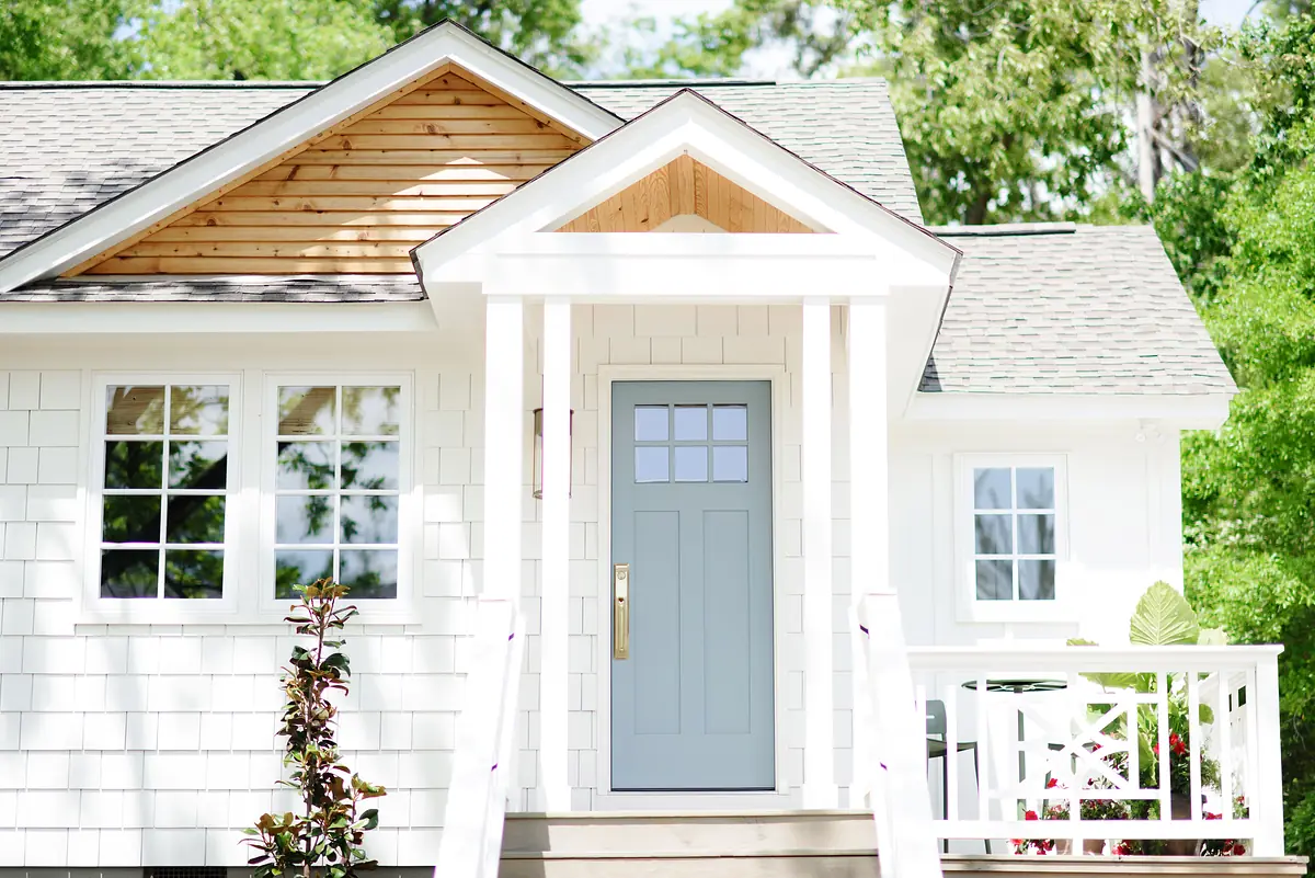 Exterior front view with light gray door, white siding, covered entryway, and greenery.