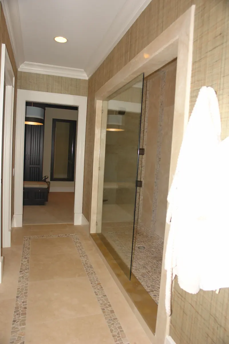 Bathroom featuring glass shower, beige tiles, towel hook, and textured wallpaper.