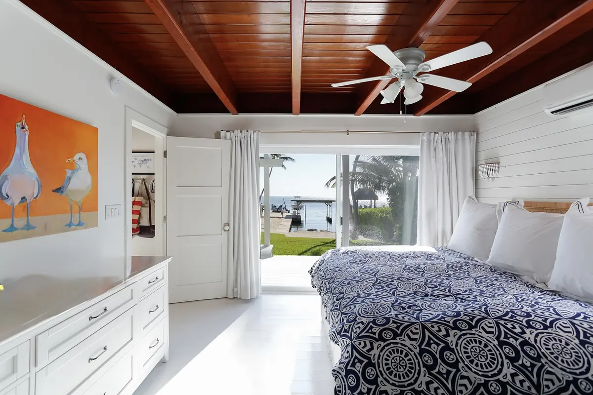 Bedroom with king-size bed, white nightstands, sliding glass door, and wooden beam ceiling.