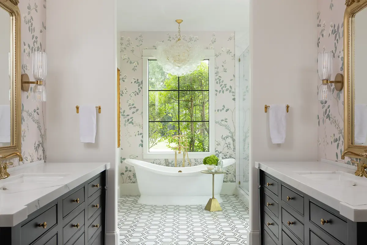 Bathroom with dual vanities, freestanding tub under window, patterned wallpaper, and geometric floor tiles.