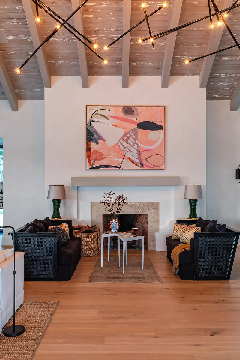 Living room with black armchairs, coffee table, area rug, colorful artwork, and exposed wooden beams.