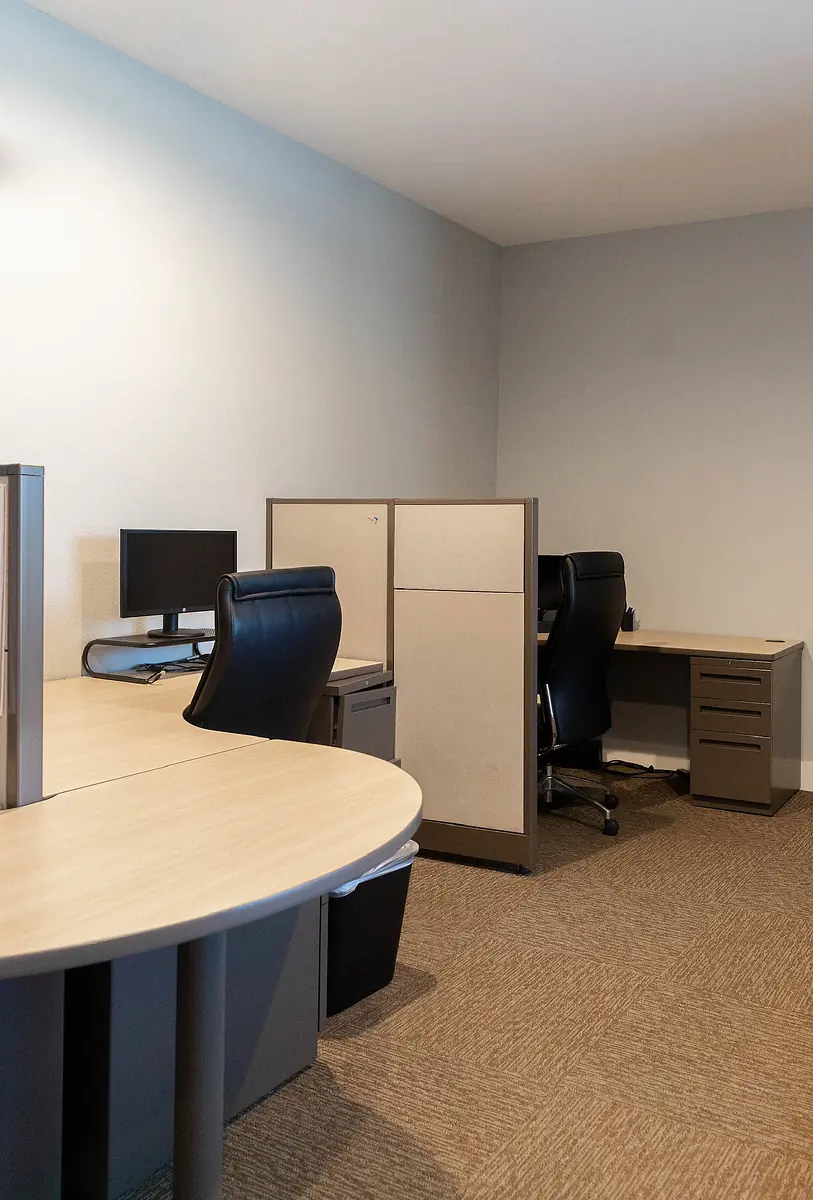 Office with two workstations, curved desks, black chairs, and desktop computers in a light-colored room.