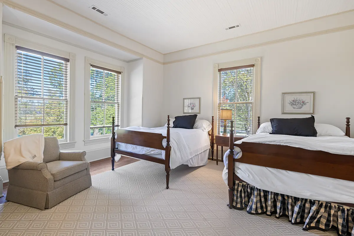 Bedroom with two wooden beds, gray armchair, side table, and patterned carpet.