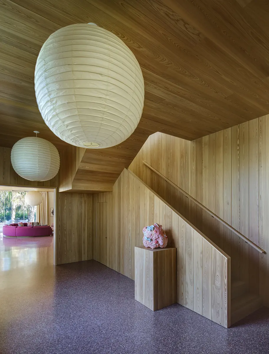 Foyer with wooden walls, staircase, light fixture, and sculpture on pedestal leading to colorful living space.
