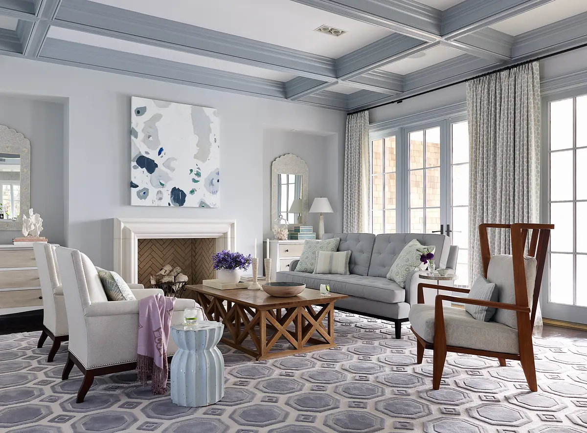 Living room with gray sofa, wooden coffee table, patterned rug, chairs, fireplace, and coffered ceilings