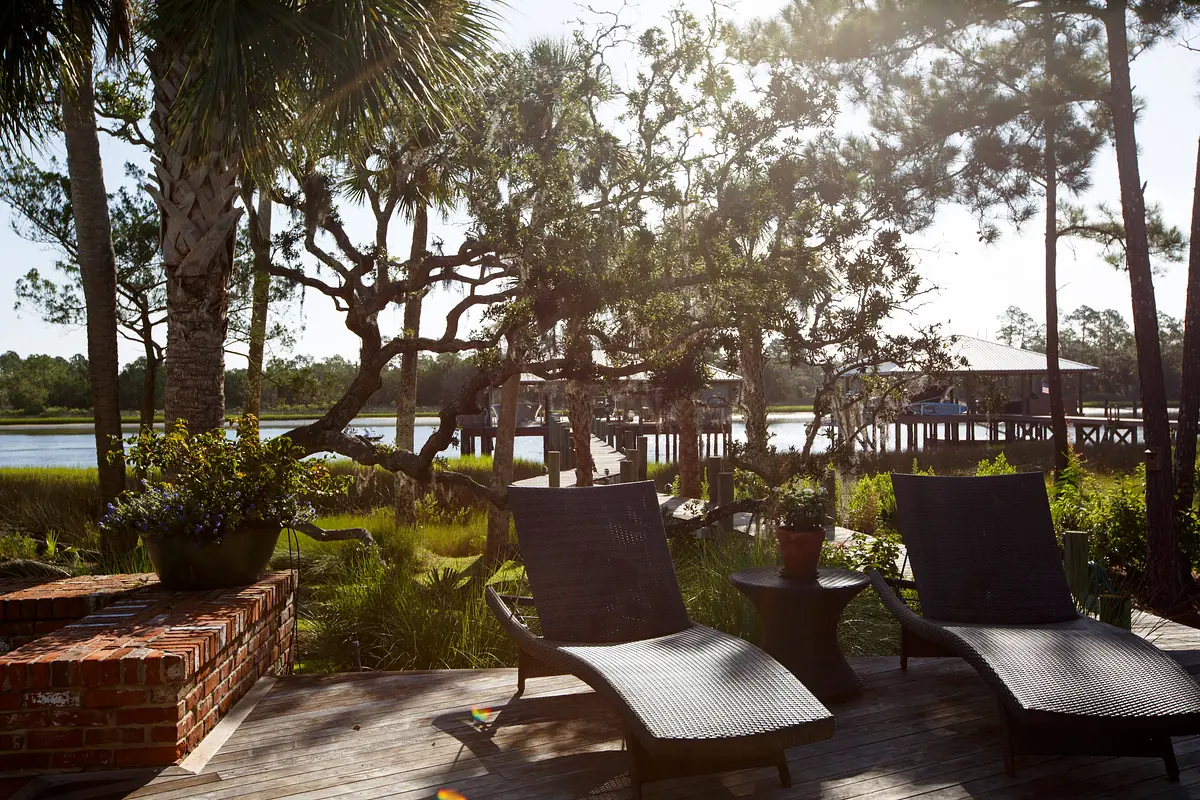 Patio with two lounge chairs, small table, potted plants, and a view of the water and trees.
