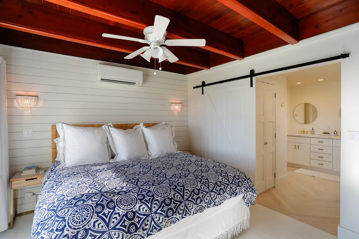 Bedroom with wooden bed, blue quilt, wall sconces, ceiling fan, and sliding barn door to bathroom.