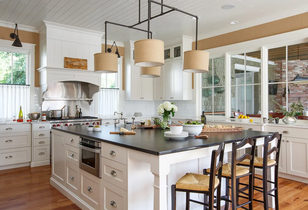 Kitchen with island, white cabinets, stainless steel appliances, and black chairs at the countertop.