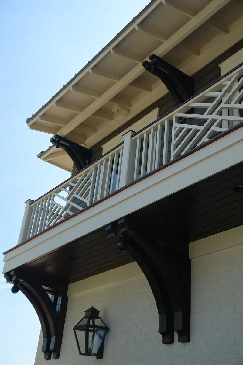 Exterior view with porch, white railing, decorative supports, and a lantern fixture.