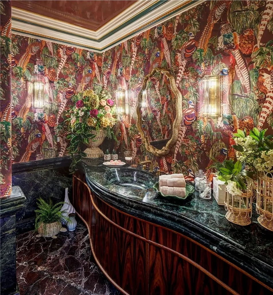 Bathroom with dark green stone countertop, floral wallpaper, wood vanity, and decorative plants.
