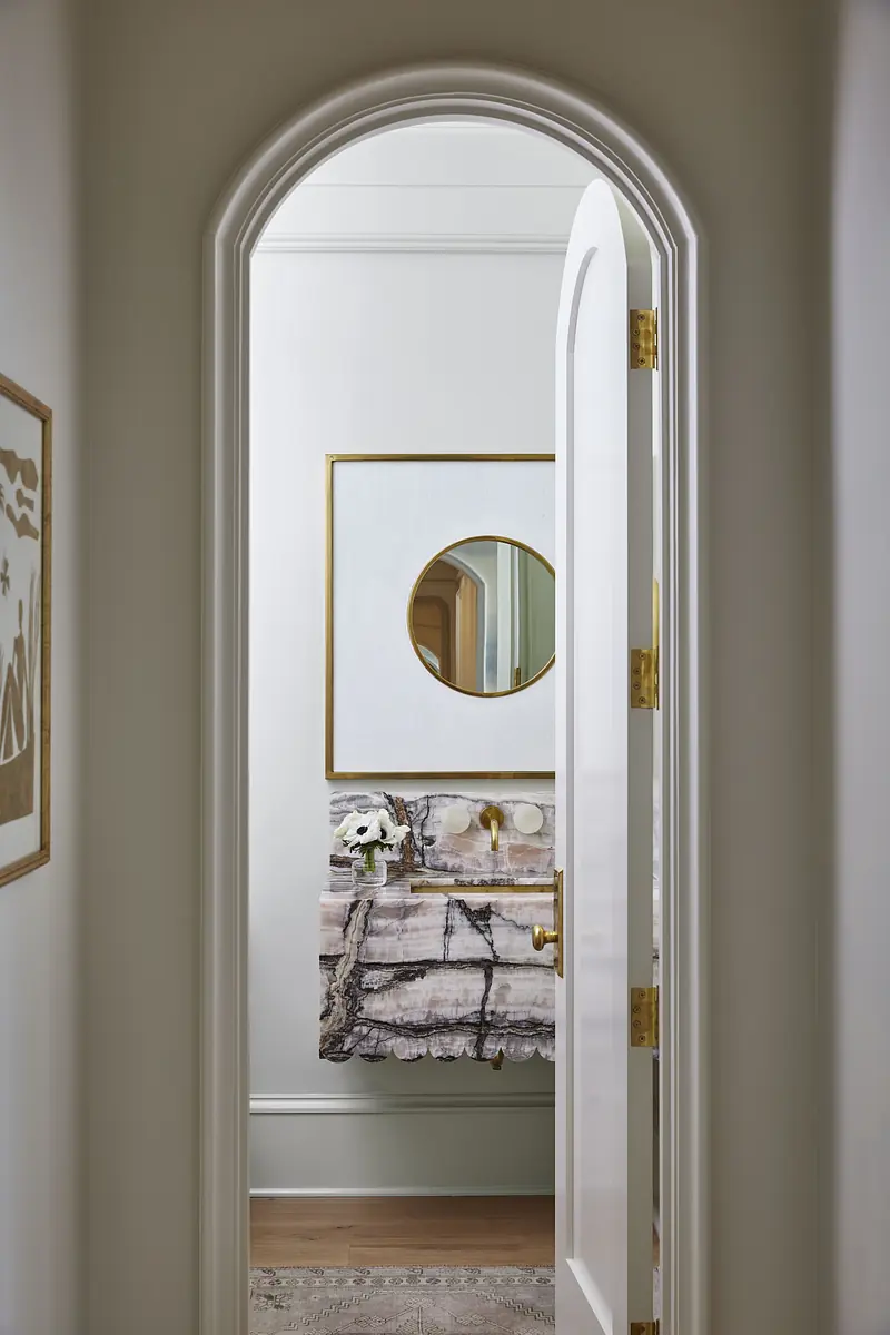 Powder room with marble counter, circular mirror, wall art, and patterned area rug.