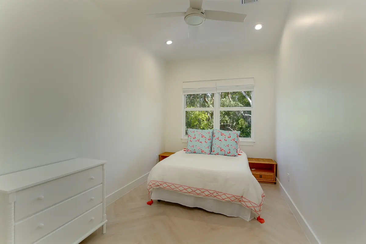 Bedroom with white bed, decorative pillows, white dresser, and two windows for natural light