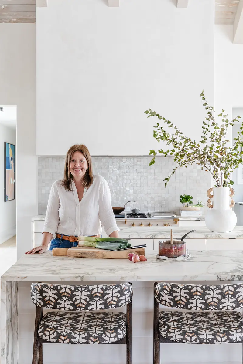 Kitchen with marble island, patterned bar stools, white cabinetry, and gray backsplash with cooking items.