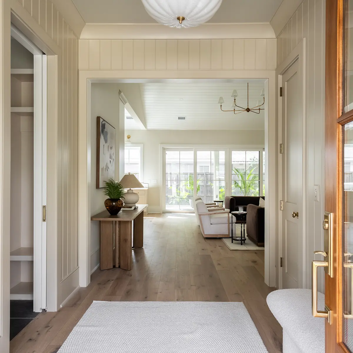Foyer with wooden paneling, white area rug, side table with lamp, and view to living area.