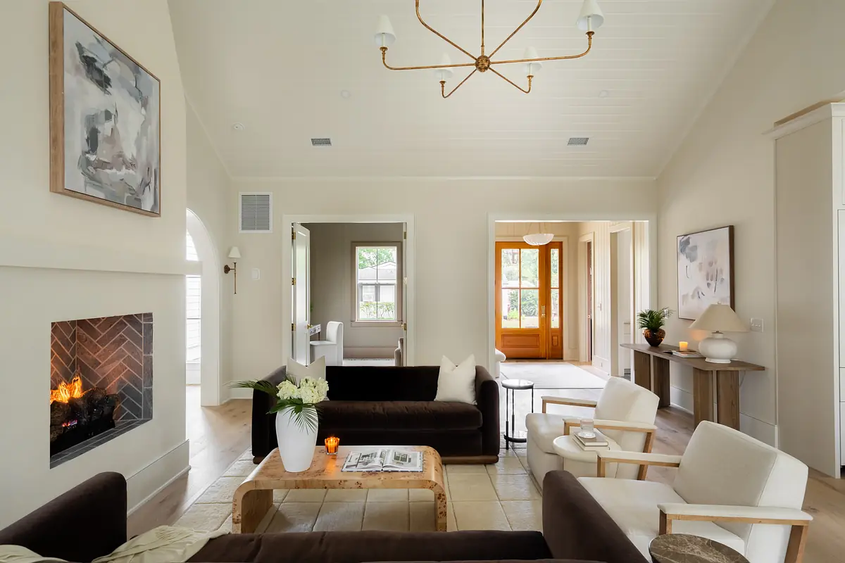 Living room with dark sofas, cream armchairs, wooden coffee table, fireplace, and large windows.