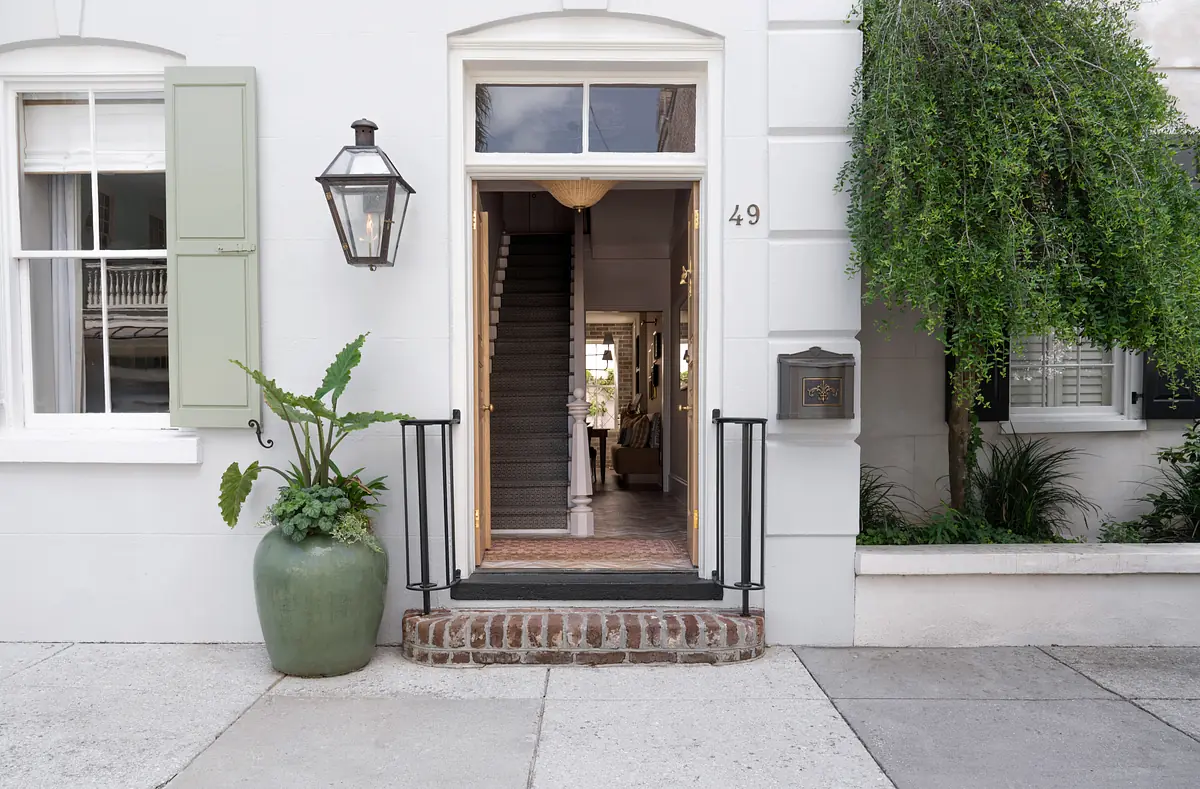Exterior front view with white facade, green shutters, lantern, brick step, and ornamental planter.