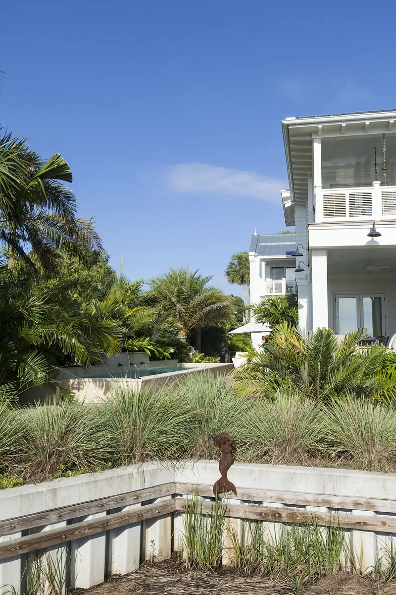 Exterior rear of a house with plants, concrete wall, metal sculpture, and balcony with large windows