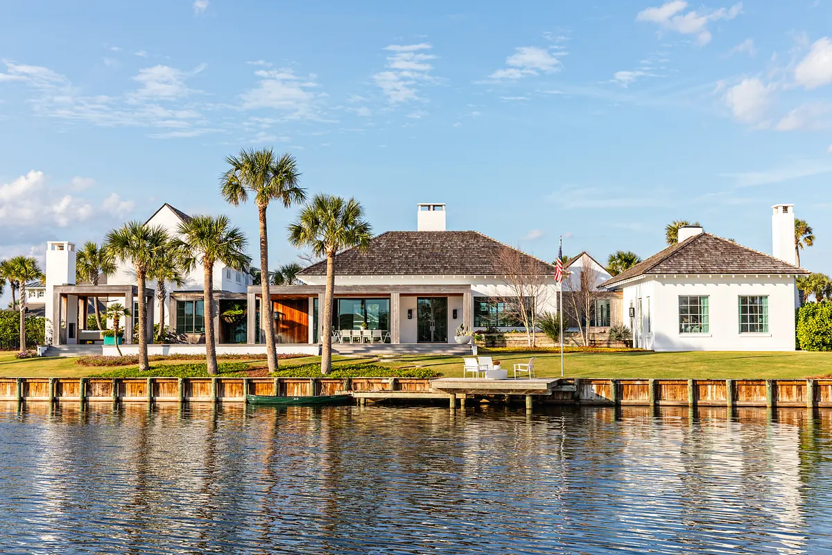 Waterfront property with three sections, dock, palm trees, and a grassy area leading to water.
