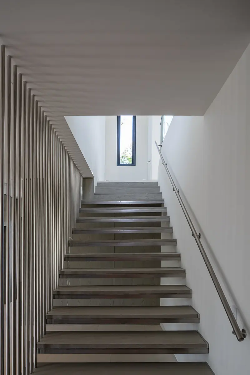 Hallway with stairs, metal railing, wooden slats, and vertical window for illumination.