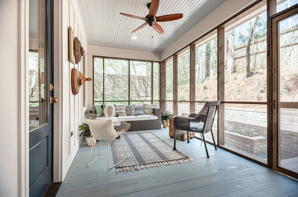 Screened porch with gray wicker seating, patterned rug, ceiling fan, and wooden walls.