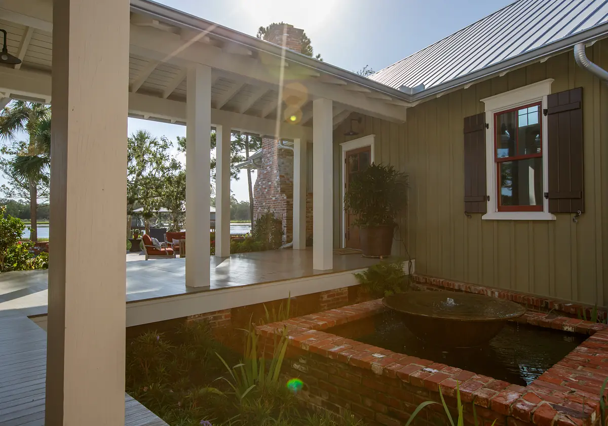 Exterior front area with covered porch, wooden beams, brick fountain, and landscaped plants.