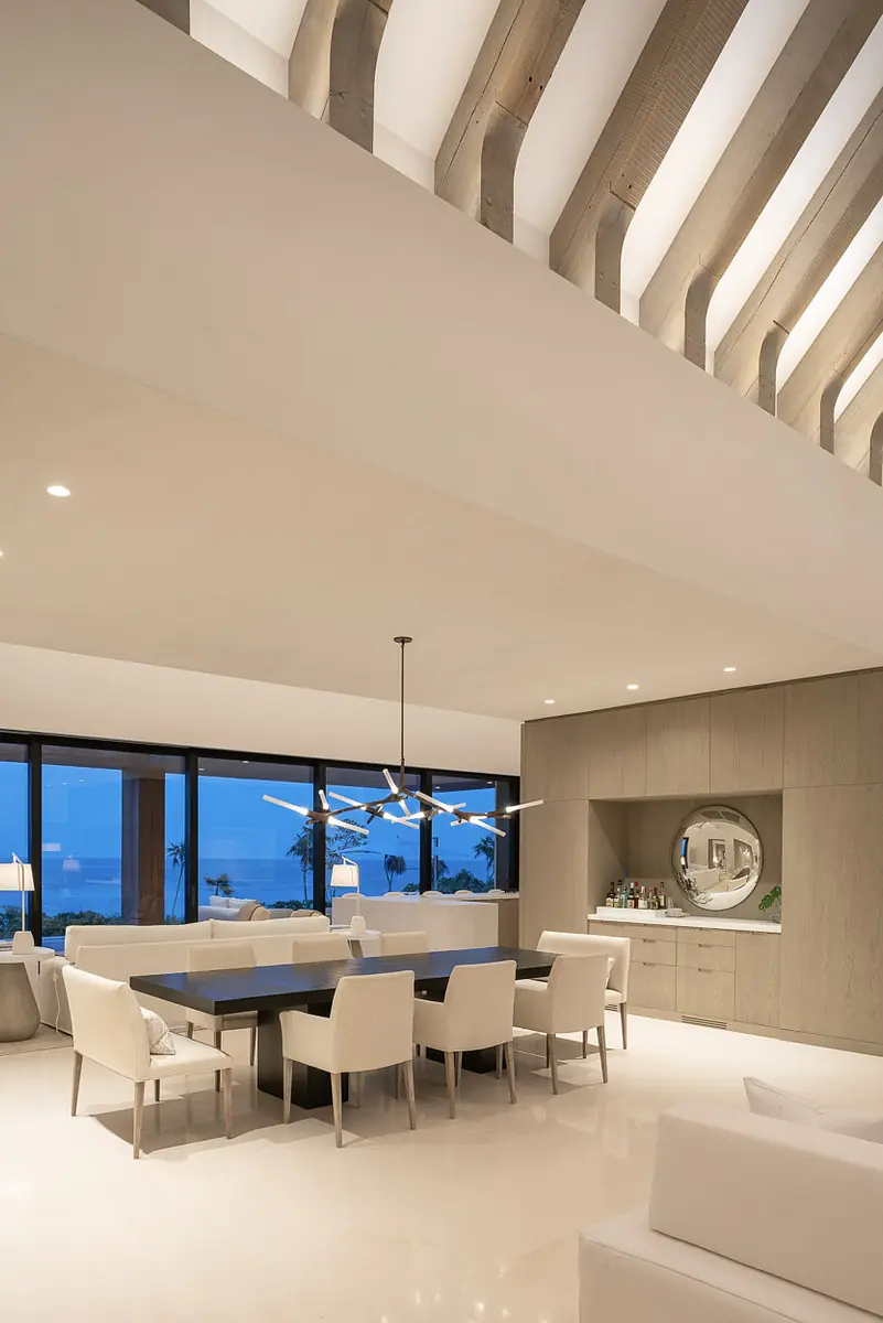 Dining room with large table, white chairs, wall mirror, built-in cabinet, and exposed beam ceiling.