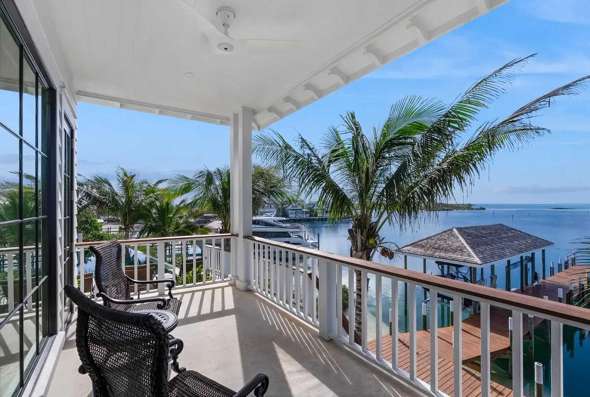 Deck with black wicker chairs, palm trees, water view, and light-colored concrete flooring