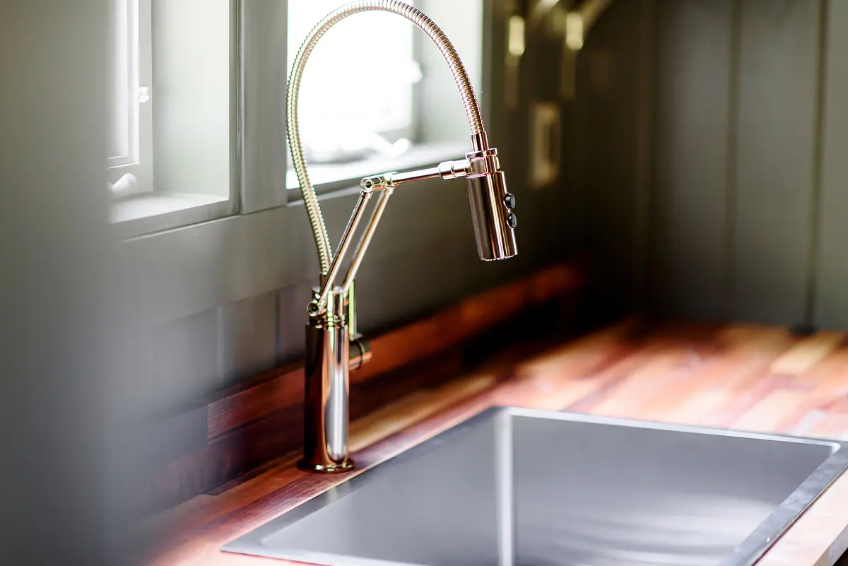 Kitchen sink area with modern faucet, stainless steel sink, and wooden countertop with natural light from windows.