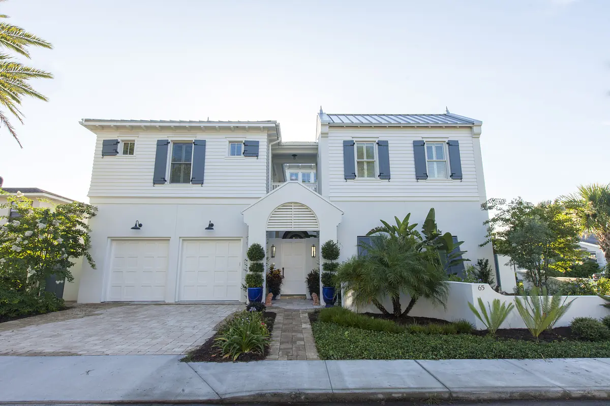 Exterior front of a house with white siding, blue shutters, arched entryway, and landscaped garden.