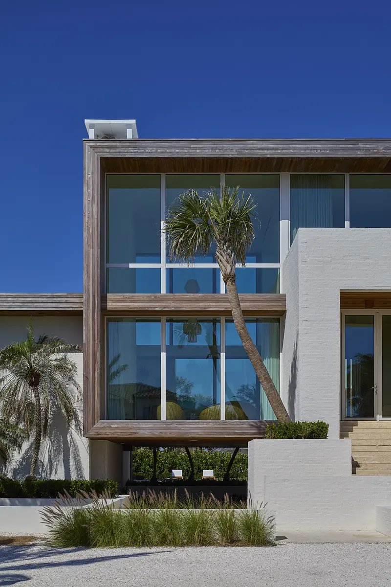 Exterior front view of a house with large glass windows, wooden accents, and palm trees.