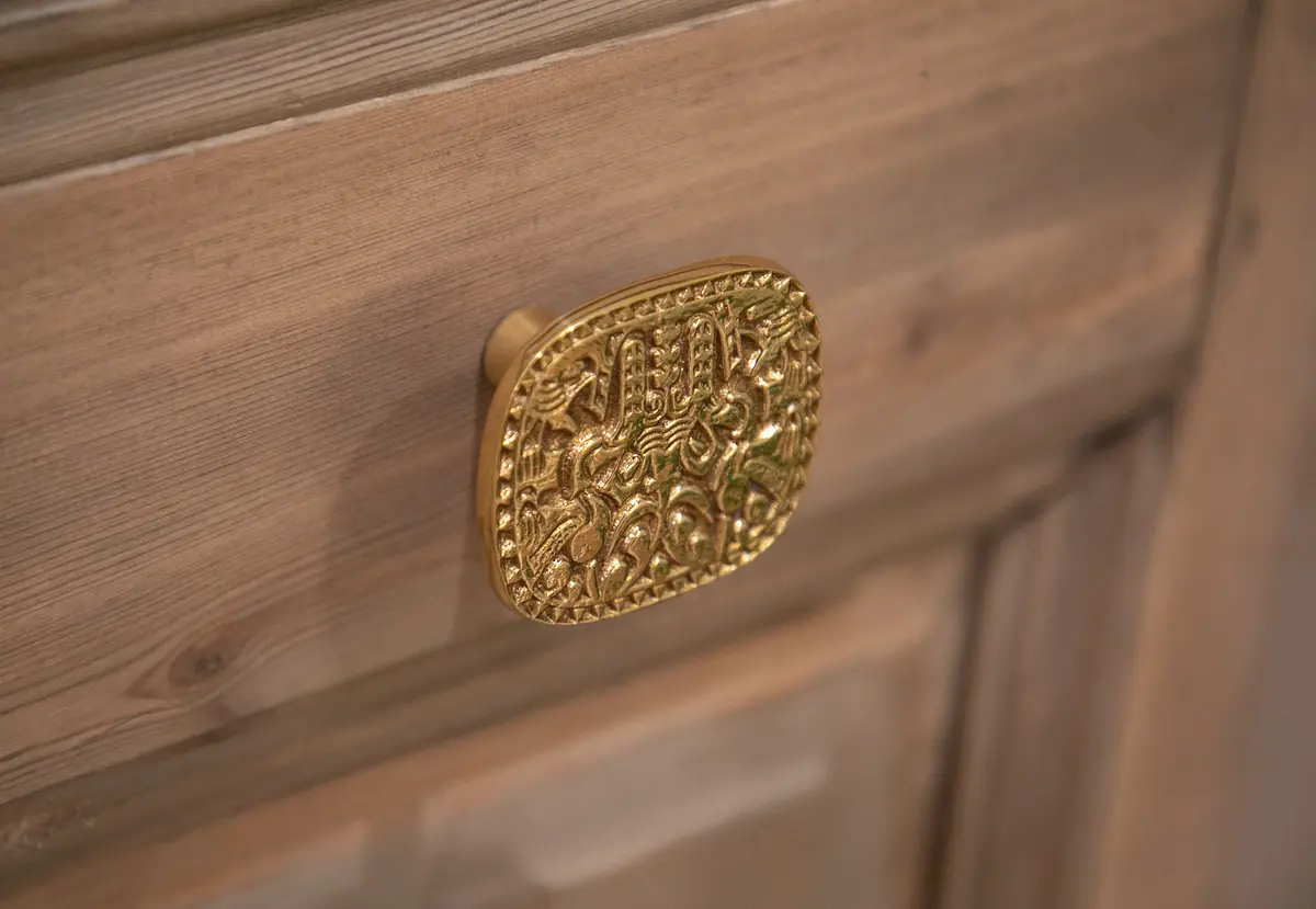 Close-up of textured wood with a gold decorative knob featuring intricate patterns.