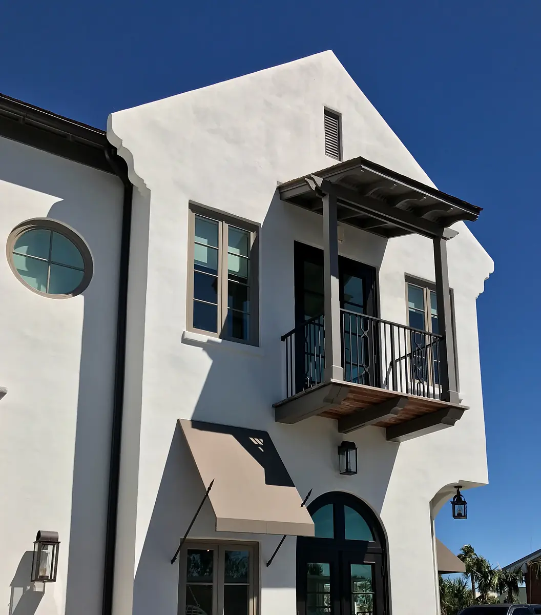 Exterior front view of a building with white stucco, balcony, large windows, and awning.