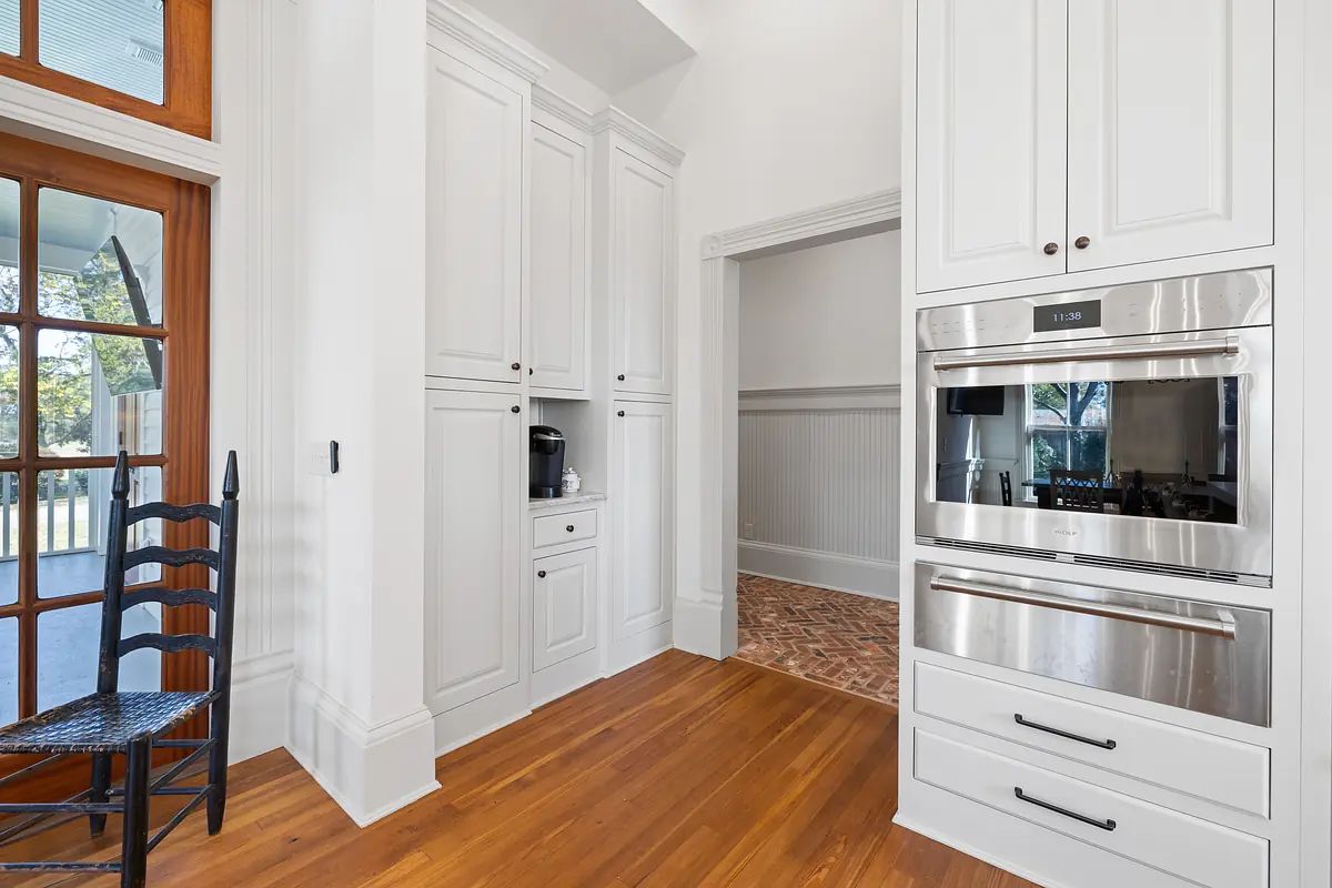 Kitchen with built-in cabinetry, stainless steel oven, black chair, and herringbone flooring.