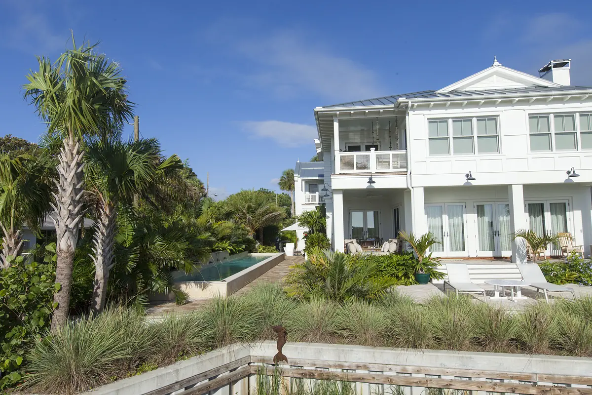 Exterior rear view of a two-story house with large windows, balcony, palm trees, and a swimming pool.